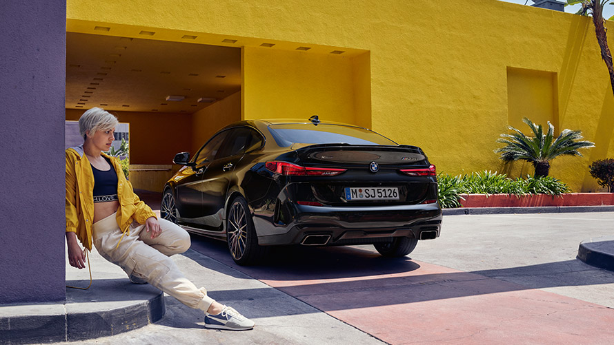 BMW M235i xDrive Gran Coupé Black Sapphire metallic F44 three-quarter rear view with woman in the front