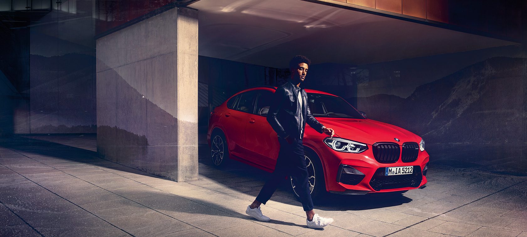 BMW X4 M Competition in Toronto Red metallic, exterior, three-quarter side view with young man.