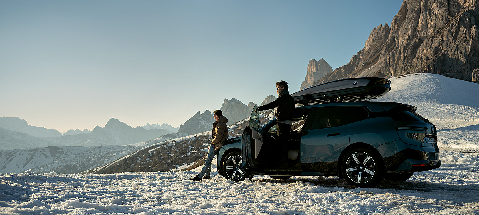 Original BMW Accessories and BMW Service for autumn and winter Men with BMW iX in snowy landscape